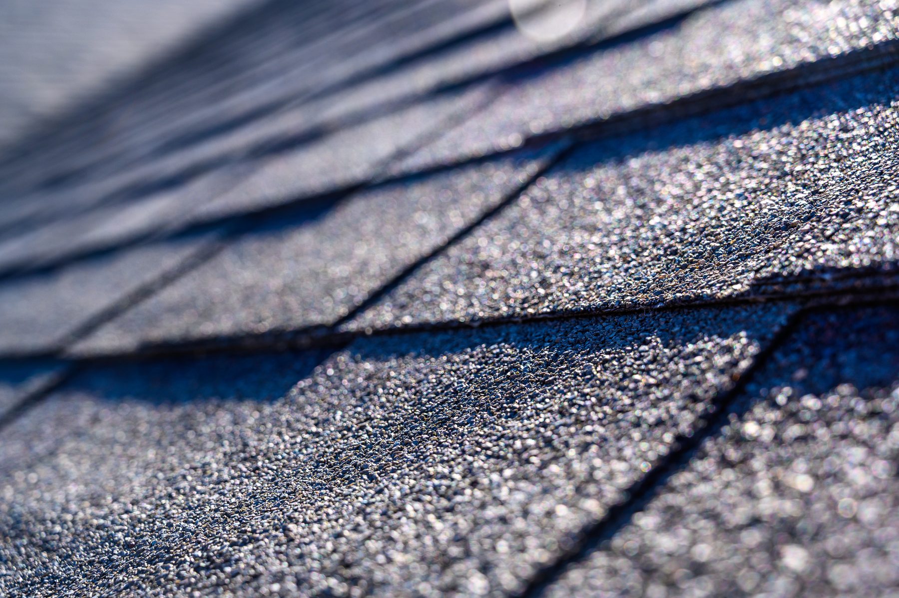 Macro view of architectural asphalt shingle courses showing the granule surface in raking sunlight