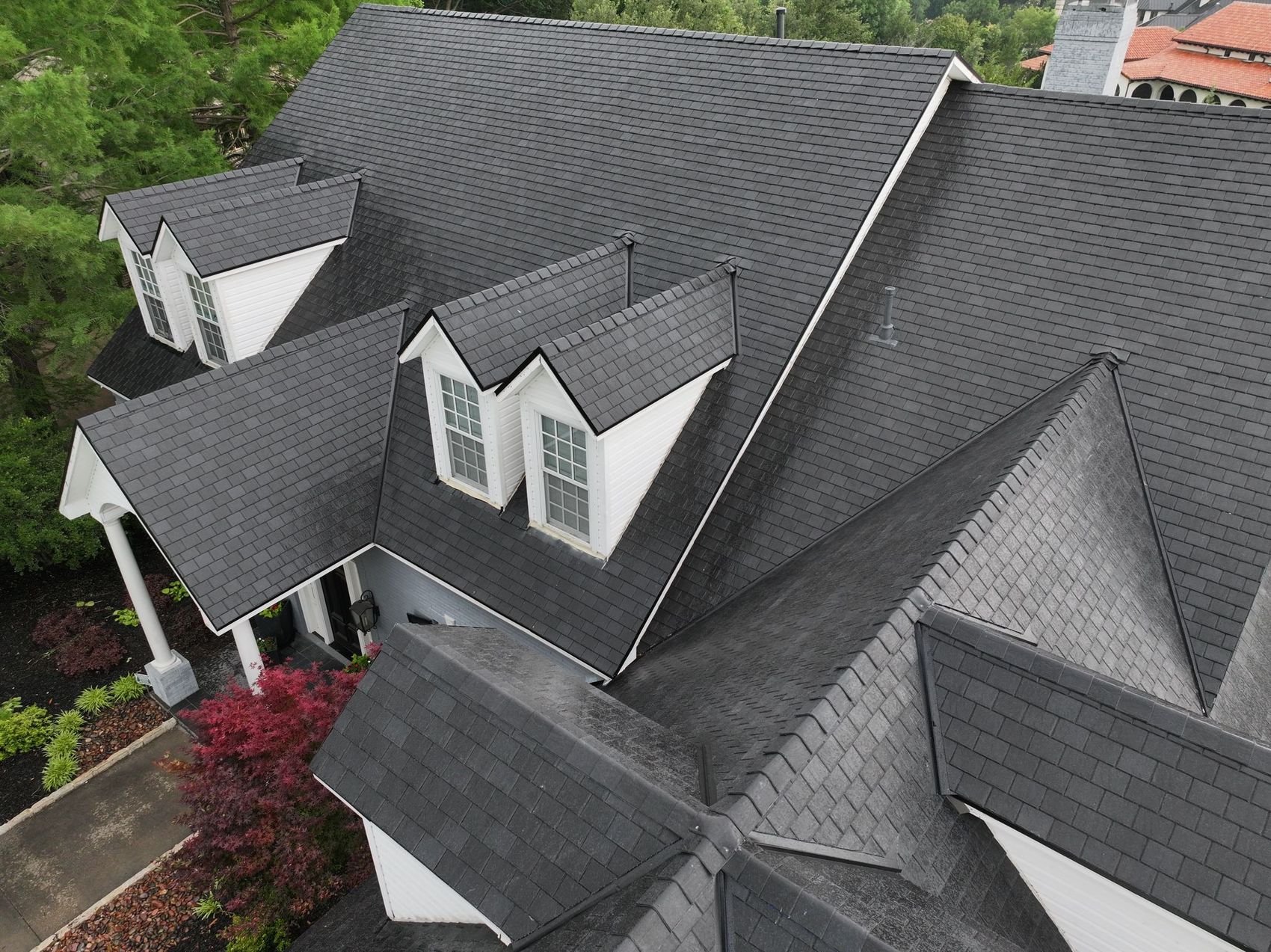 Aerial view of a steep black slate-look shingle roof with multiple gables and dormers on a large home