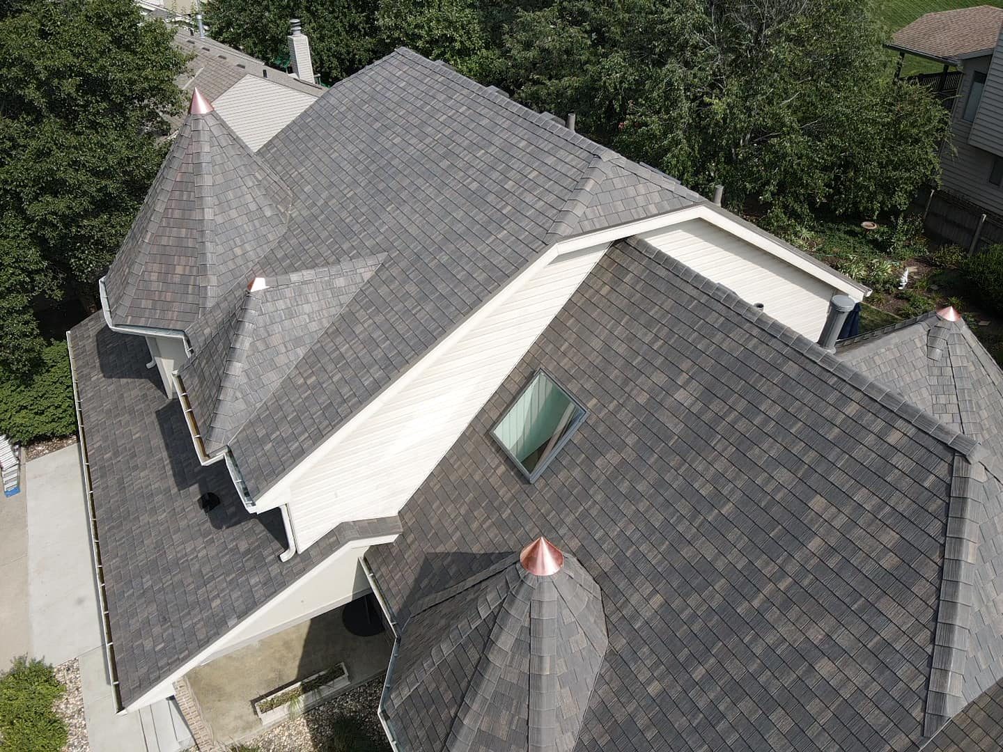 Aerial view of a complex slate-look shingle roof with copper-capped turrets on a large home
