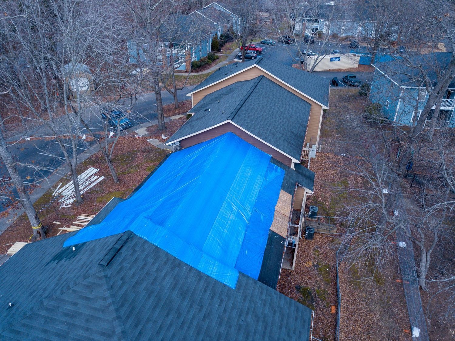 Aerial view of a storm-damaged roof covered with a blue emergency tarp while repairs are scheduled
