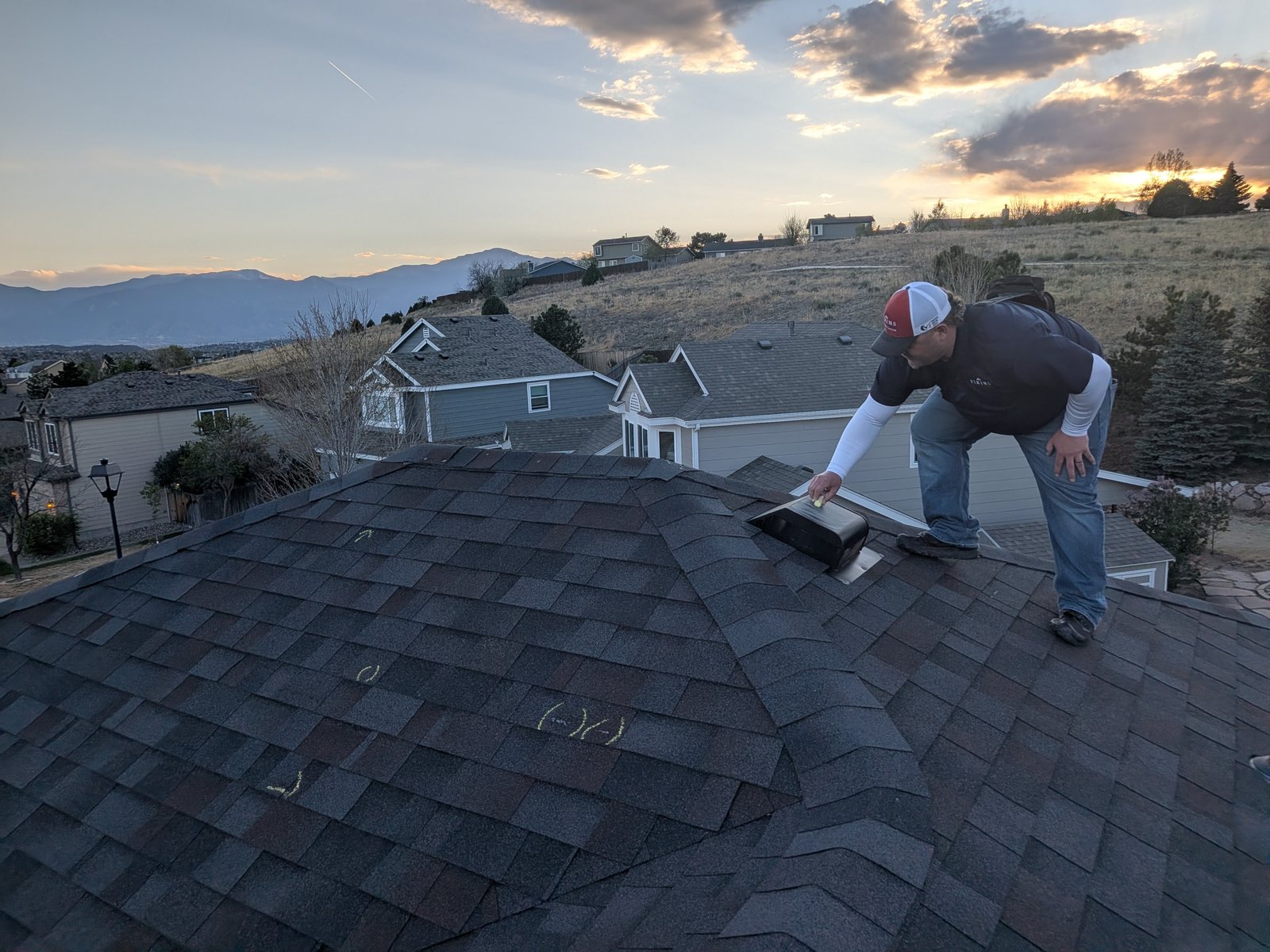 Fixins inspector examining a roof vent and marked storm damage above Colorado Springs at sunset